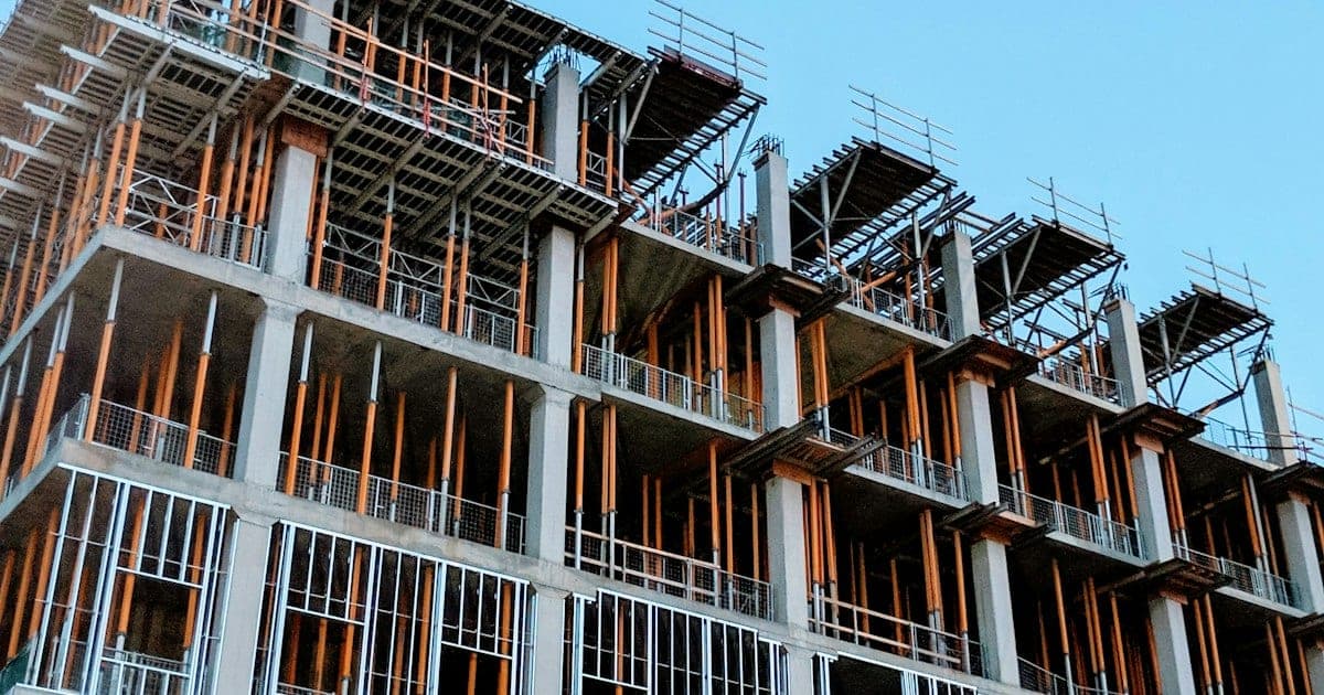 Struttura in cemento di un edificio a più piani in costruzione con puntelli arancioni e casseforme