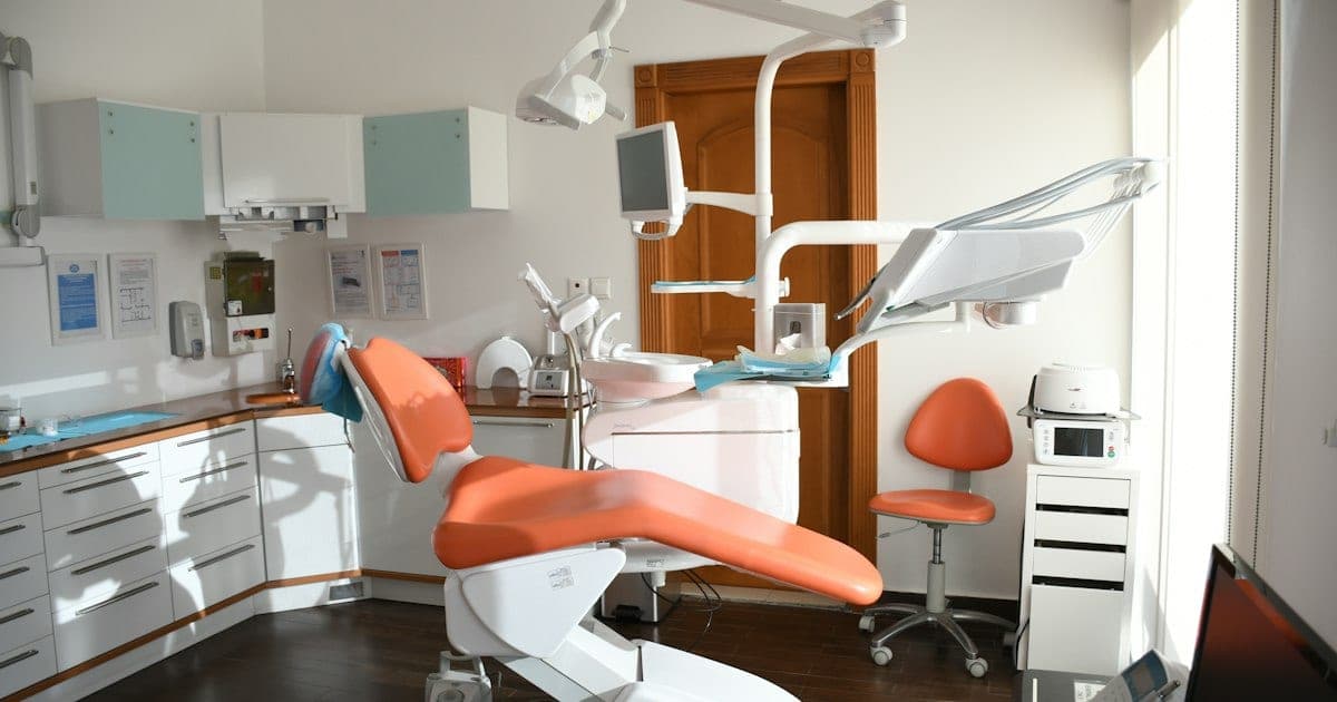 Cabinet dentaire vide avec fauteuil de soins orange, scialytique et plateau d'instruments près d'une fenêtre ensoleillée