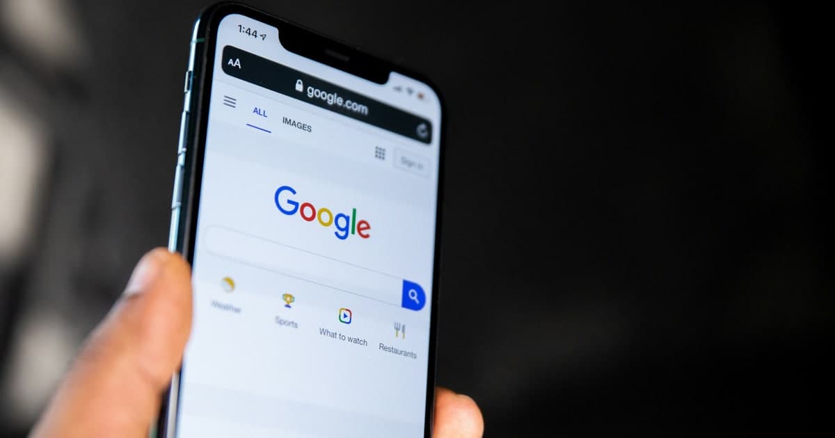 يد تمسك هاتفًا يعرض الصفحة الرئيسية لبحث Google بمربع بحث فارغ