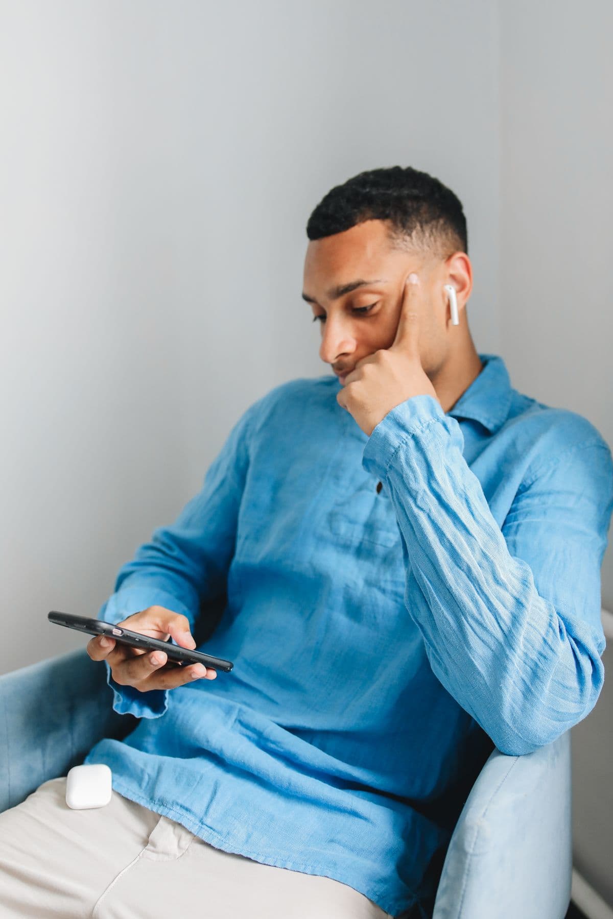 Man in blue shirt using smartphone while wearing wireless earbuds indoors