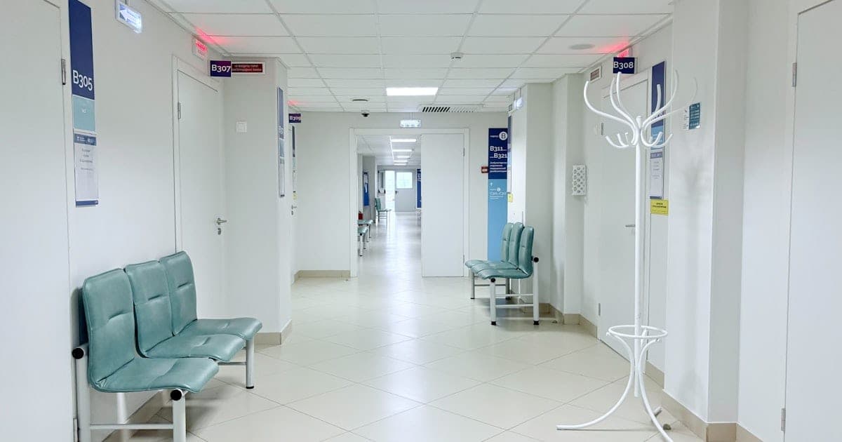 Couloir vide d'une clinique avec portes de salles de consultation numérotées et bancs d'attente vert pâle