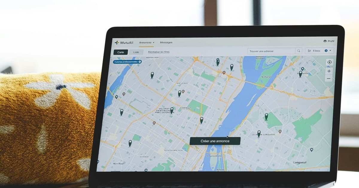 A laptop open on a desk showing a city street map covered in dark location pins
