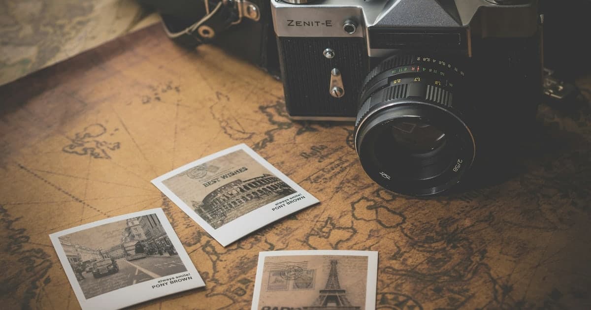 A vintage film camera and three printed travel photos lying on an old world map