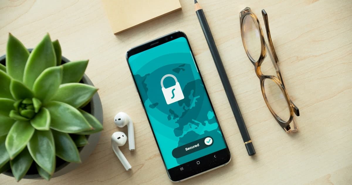A phone on a desk showing a white padlock over a teal world map with the word Secured