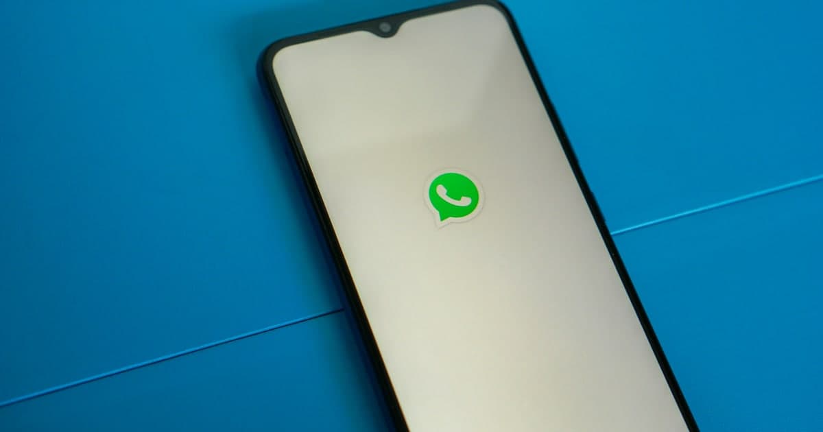 A smartphone lying on a blue surface showing the green WhatsApp logo on its screen