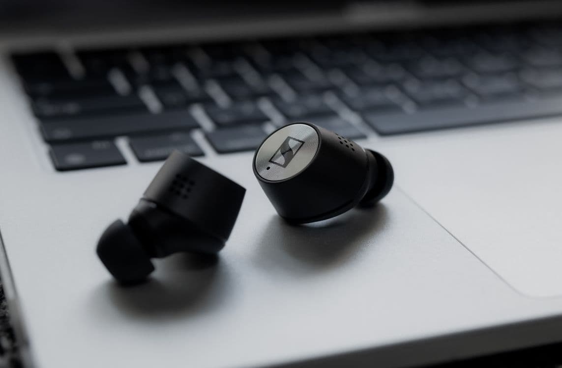 Black wireless earbuds resting on a silver laptop keyboard. Photo by Spot Wizard Lee on Pexels